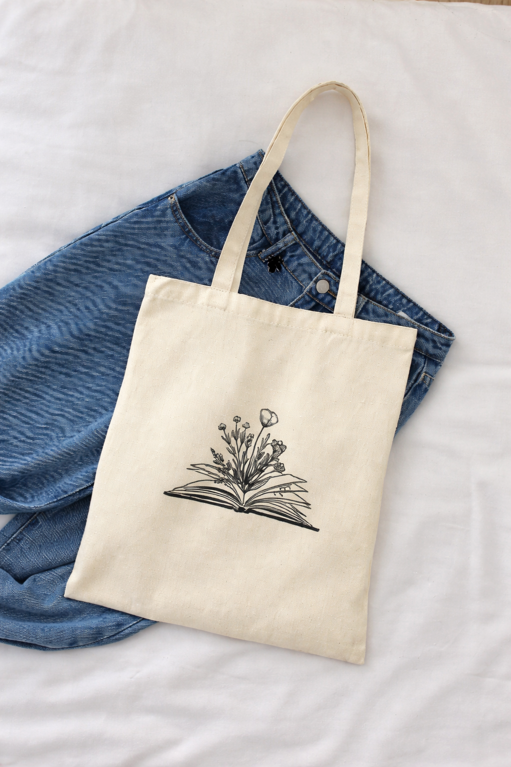 Beige tote bag with floral design on a blue denim jacket on a white surface