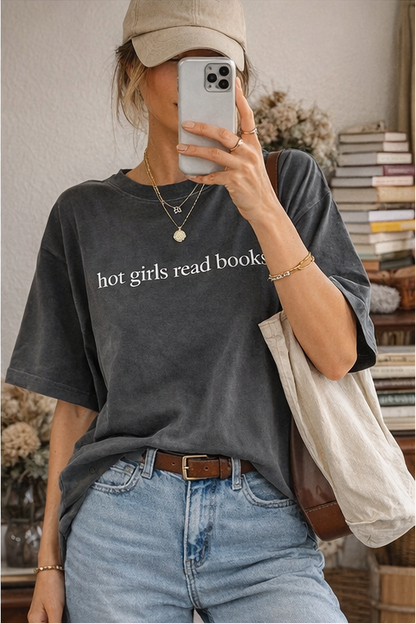 Person wearing a dark gray t-shirt with 'hot girls read books' text, holding a phone.