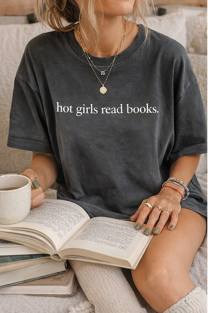 Person wearing a black t-shirt with 'hot girls read books.' text, holding a mug and an open book.